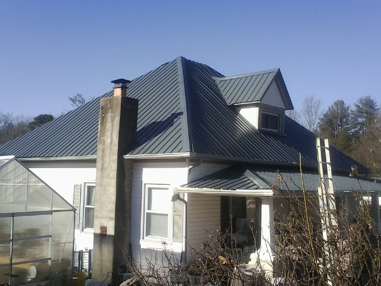 Dark blue standing seam metal roof on a white farmhouse with dormer — Slate & Tile Roof Repair by Roofing Brothers in Chippewa Lake