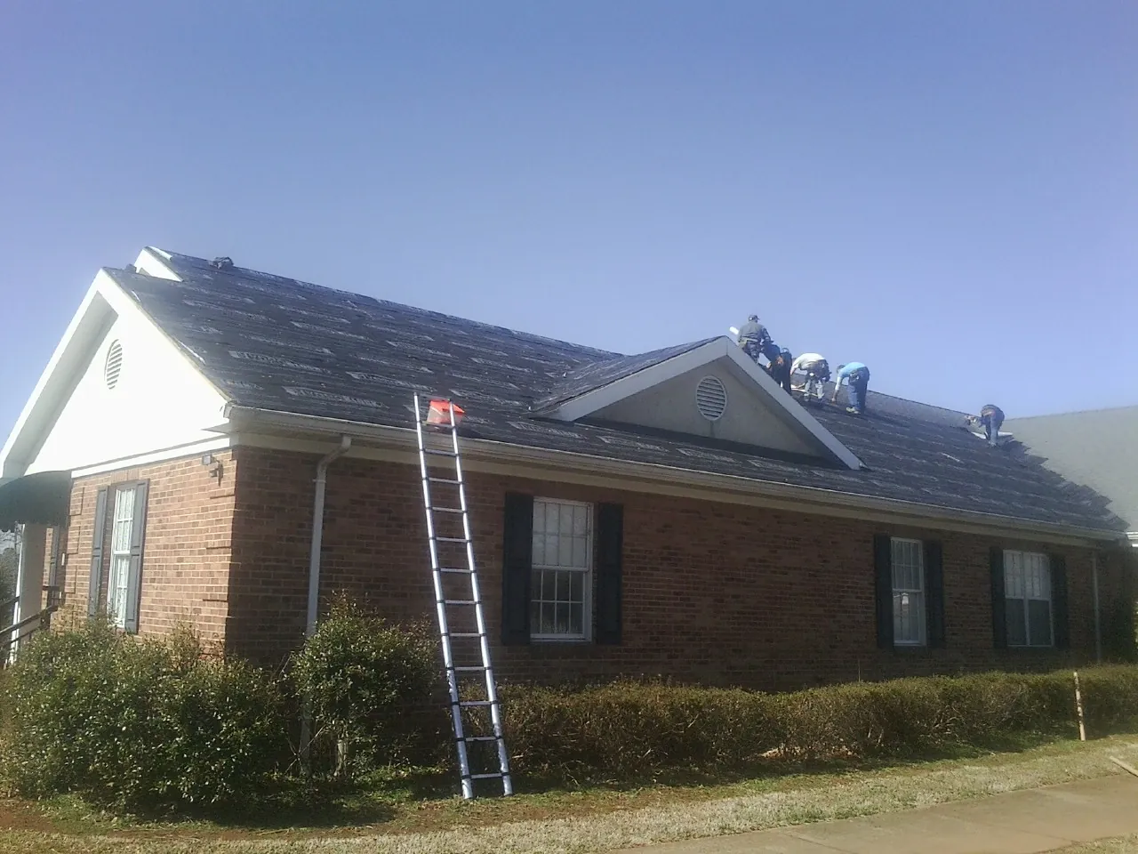 Crew tearing shingles off a brick ranch roof with a ladder set — Metal Roof Repair work by our crew in Chippewa Lake