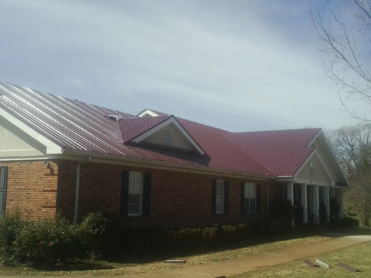 Red metal roof with gabled entries on a long brick building, from a Hail Damage Roof Repair job in Chippewa Lake