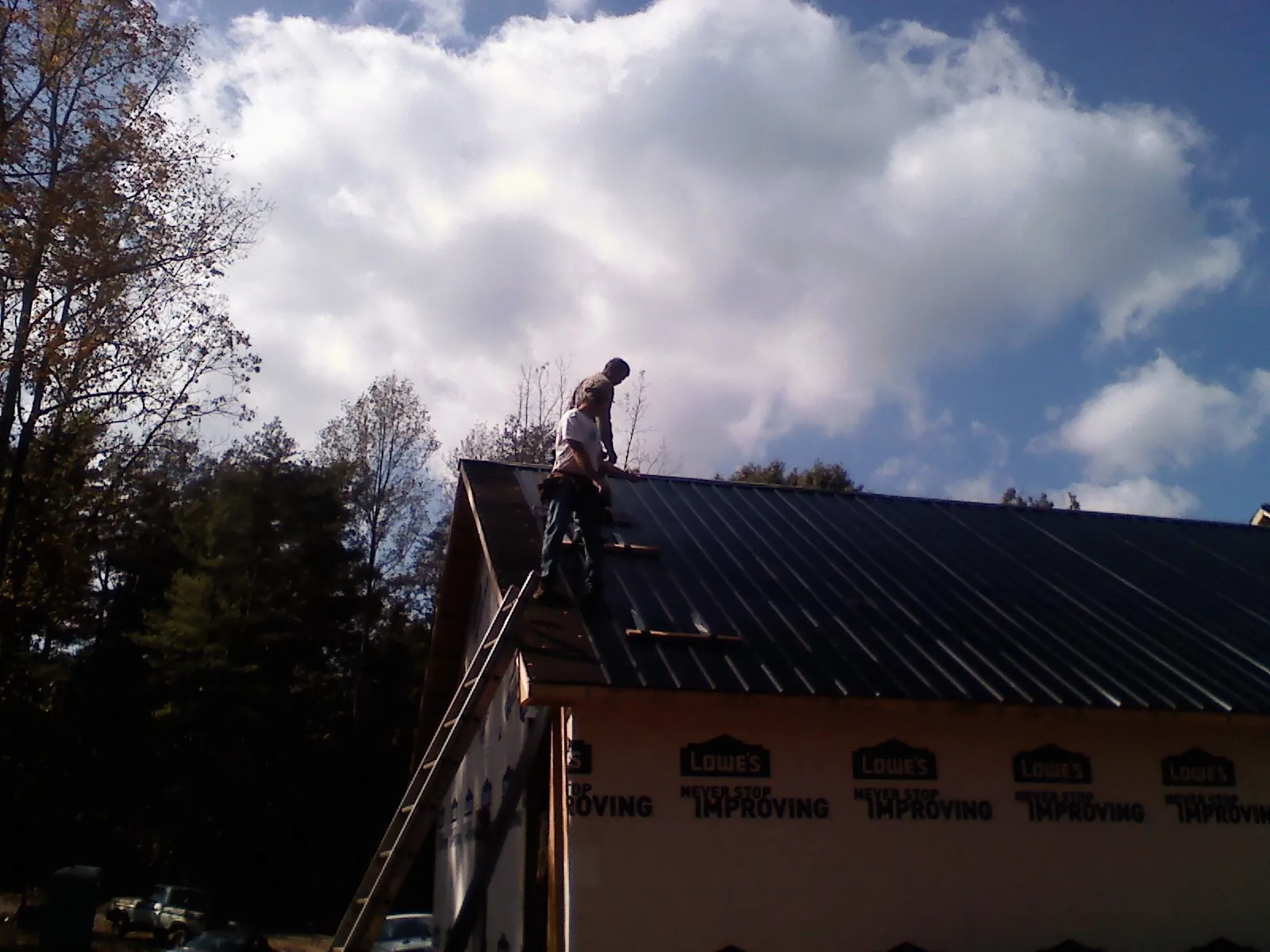 Roofer fastening dark metal panels high against a cloudy sky, from a Roof Inspection job in Chippewa Lake