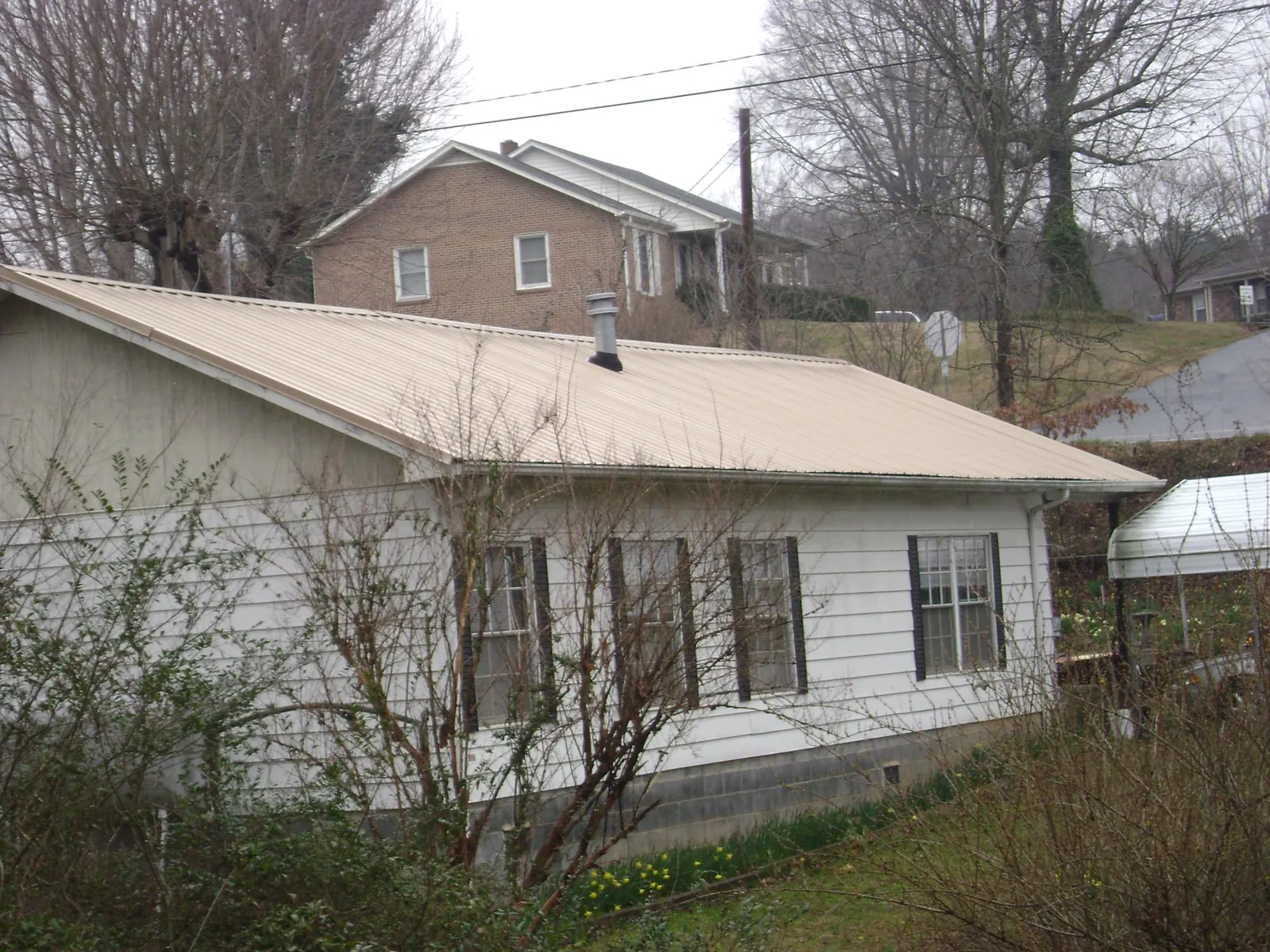 Tan metal roof on a white sided house set into a hillside — Commercial Roofing by Roofing Brothers in Chippewa Lake