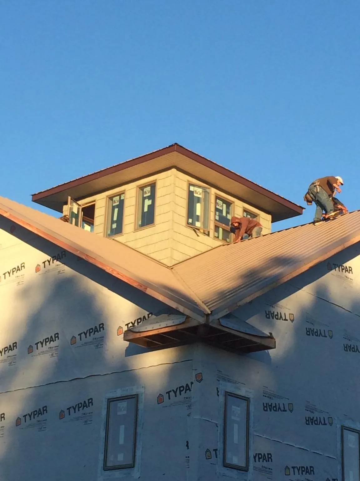 Roofers working around a rooftop cupola on a new metal roof at sunset in Chippewa Lake